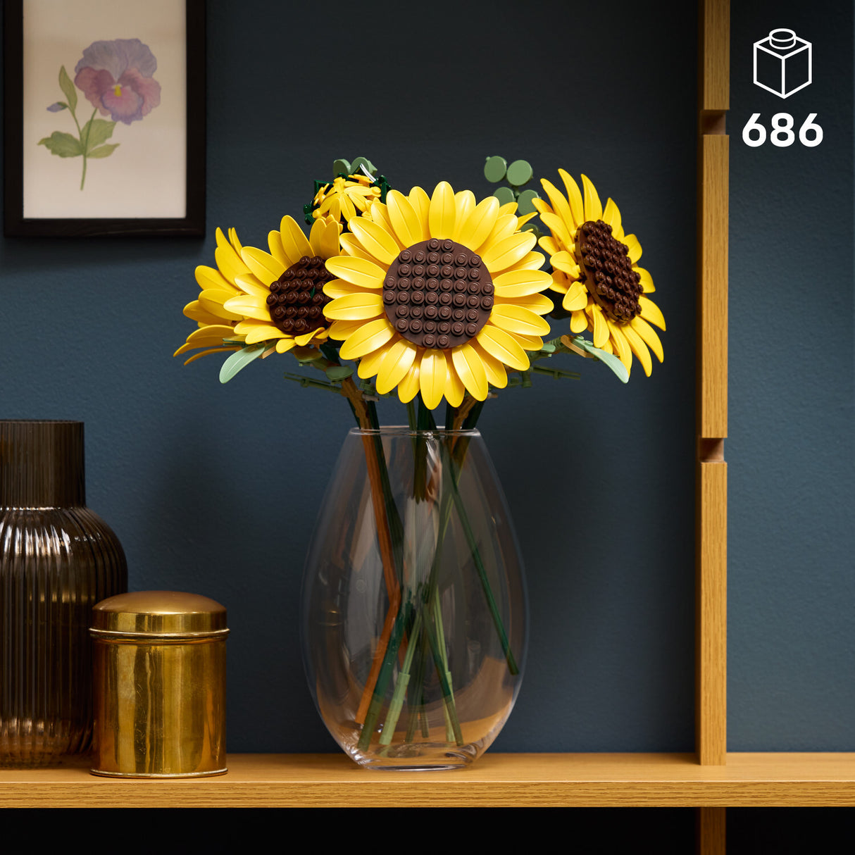 Clear vase with LEGO Botanicals: Sunflower Bouquet on a wooden shelf against a dark blue wall.