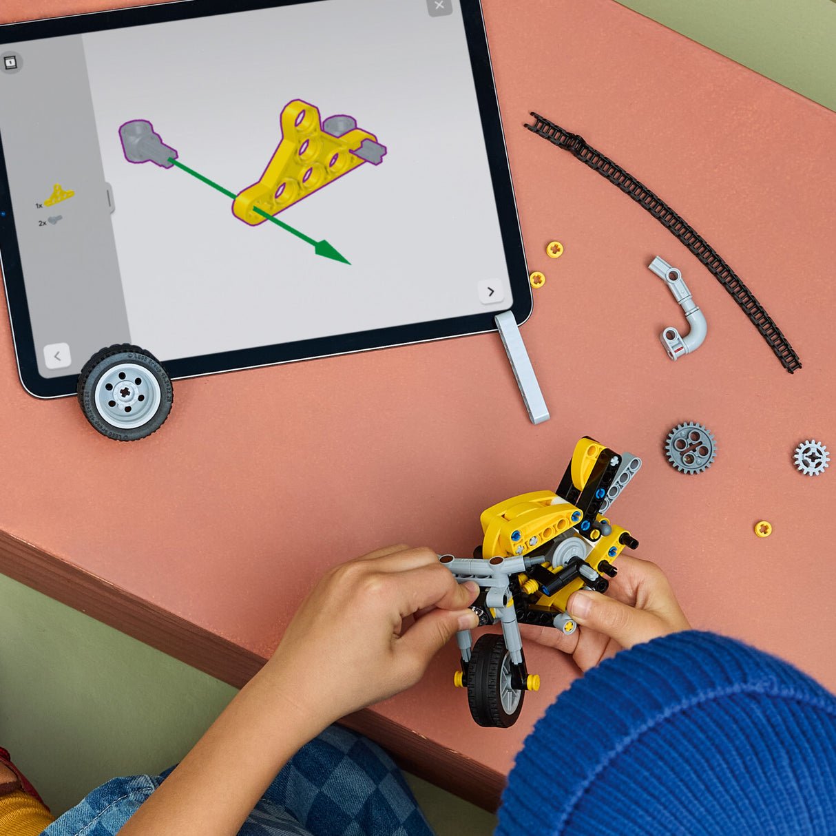 Child playing with a LEGO Technic: Yellow Motorcycle set on a table with a tablet displaying a design.