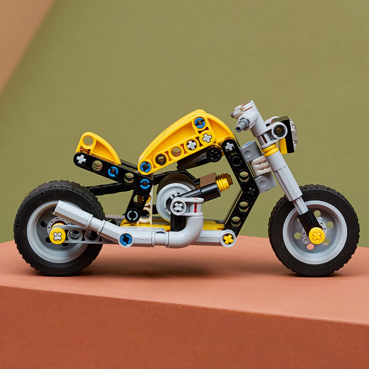 LEGO Technic: Yellow Motorcycle toy made of interlocking bricks on a brown surface with a green background