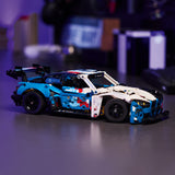 Toy LEGO Technic: BMW M4 GT3 EVO Race Car made of interlocking bricks on a reflective surface with a blurred background