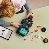 Child building a toy LEGO Technic: Jeep® Wrangler Rubicon SUV with scattered parts on a light green table.