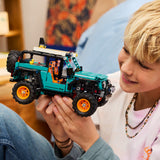 Child holding a toy LEGO Technic: Jeep® Wrangler Rubicon SUV made of interlocking bricks, with a blurred indoor background.