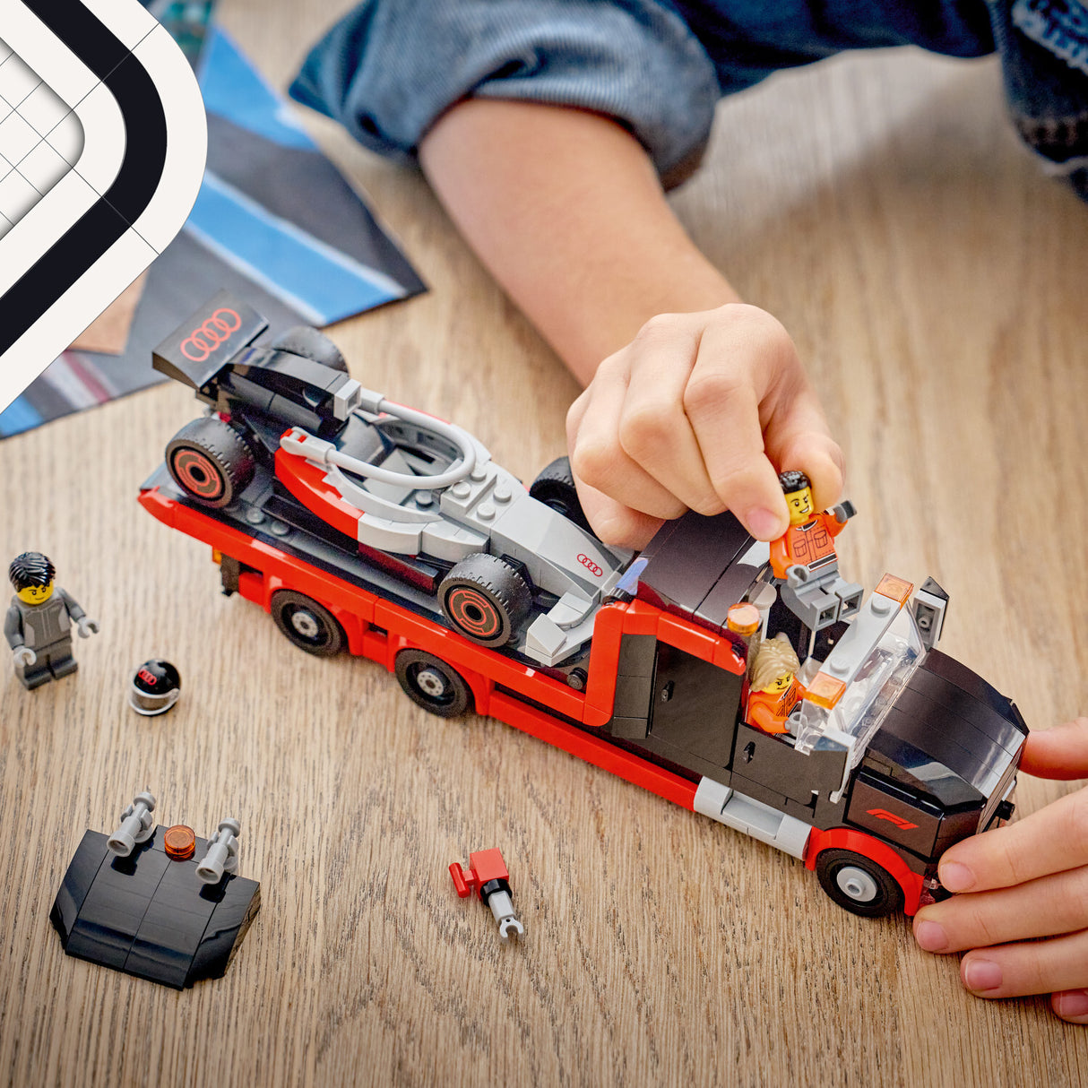 Child playing with a toy LEGO City Formula 1: F1® Display Truck with Audi F1® Race Car set on a wooden table