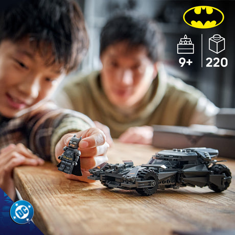 Children playing with a toy LEGO Super Heroes DC: Batman v Superman™ Batmobile™ set on a wooden table, with a Batman logo and product details in the corner.