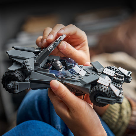 Person holding a detailed toy LEGO Super Heroes DC: Batman v Superman™ Batmobile™ model, likely made of building blocks, with a blurred background.