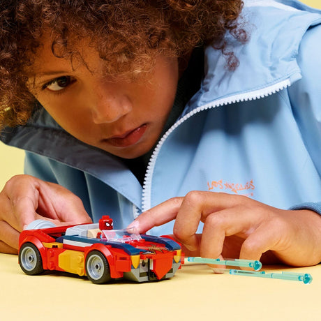 Child playing with a toy LEGO Super Heroes Marvel: Spider-Man Car vs. Venomized Wolverine kit made of interlocking bricks on a yellow surface.