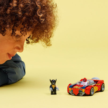 Child playing with a LEGO Super Heroes Marvel: Spider-Man Car vs. Venomized Wolverine kit and figure on a yellow background