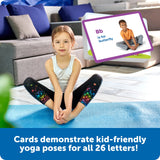 Child sitting on a blue mat with educational cards demonstrating yoga poses for letters, in a living room setting.