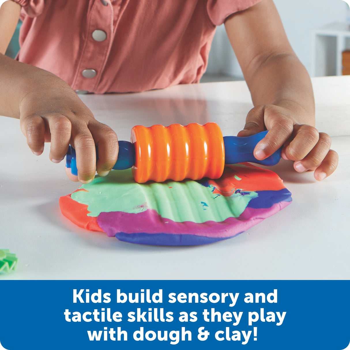 Child playing with a colorful dough roller and mold on a white surface.