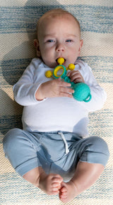 Baby lying on a striped blanket holding a Gumlii Teether Rattle