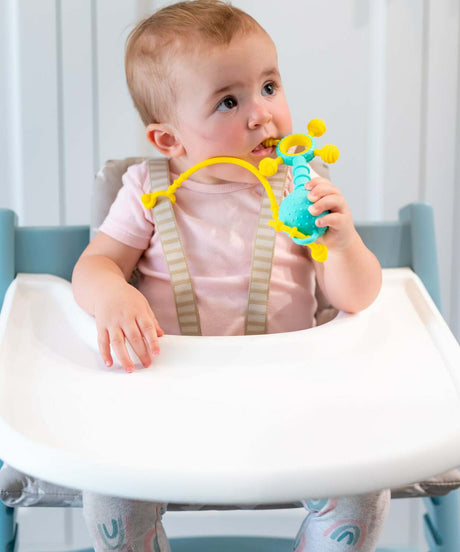 Baby in a high chair holding a Gumlii Teether Rattle