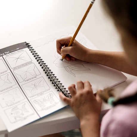 Person drawing in a Mini-Sketch Pad with a pencil on a light surface