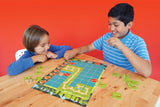 Two children playing Race To The Treasure Cooperative board game on a wooden table with a red background