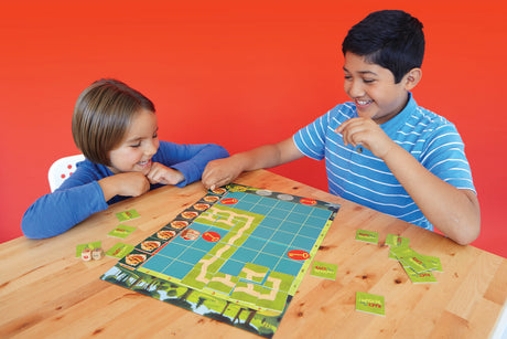 Two children playing Race To The Treasure Cooperative board game on a wooden table with a red background