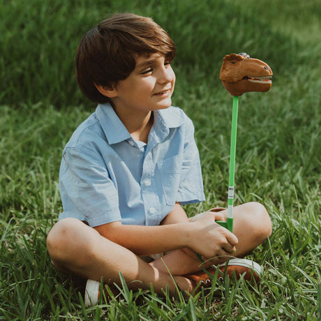 Child sitting on grass holding a Brown T-Rex Snapper Toy