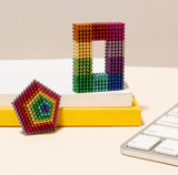 Colorful Spectrum Speks sculptures on a desk with a keyboard and books in the background.