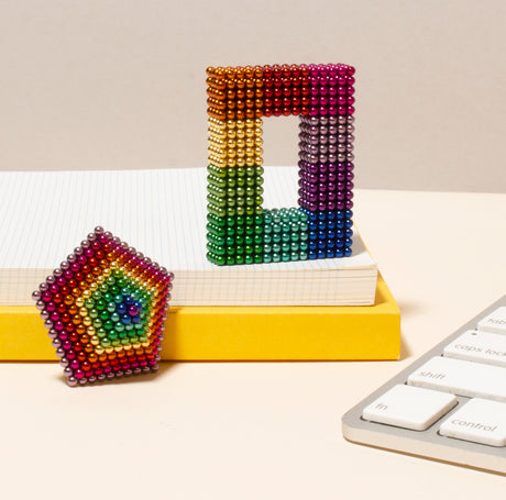 Colorful Spectrum Speks sculptures on a desk with a keyboard and books in the background.