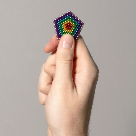 Hand holding a small, colorful Spectrum Speks structure against a gray background