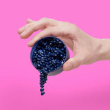 Hand holding a blue container with Mini Matte Crags Indigo against a pink background