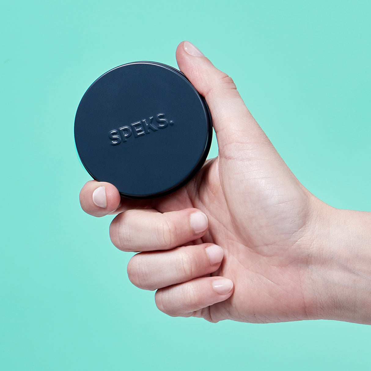 Hand holding a black Mini Crags Oil Slick container against a light blue background