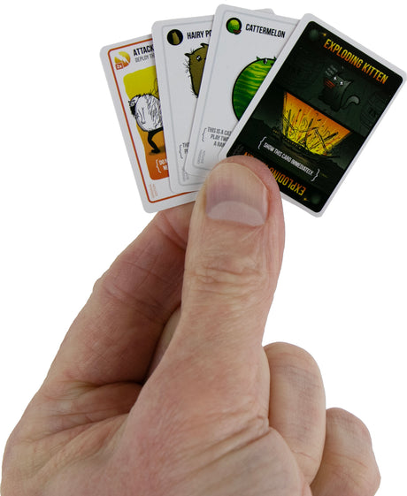 Hand holding a set of World's Smallest Exploding Kittens  cards with humorous designs on a white background