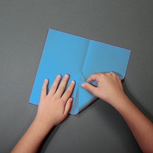 Hands folding a blue piece of paper on a gray surface
