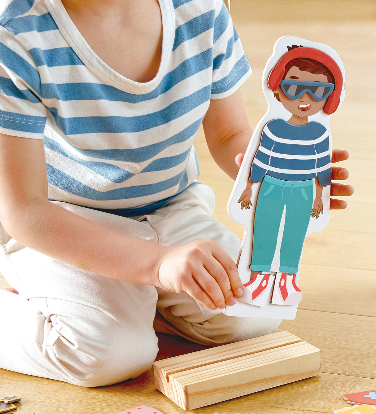 Person playing with a Dress-Up Magnetic Puzzle wooden doll on a wooden floor