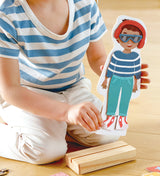Person playing with a Dress-Up Magnetic Puzzle wooden doll on a wooden floor
