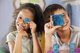 Two children holding colorful Magna-Tiles microMags Travel Deluxe 55 Piece Set up to their eyes in a classroom setting.