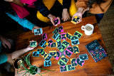 Group of people playing Tacta Card Game with colorful cards on a wooden table.