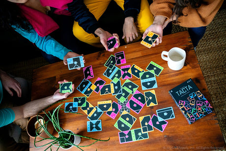 Group of people playing Tacta Card Game with colorful cards on a wooden table.