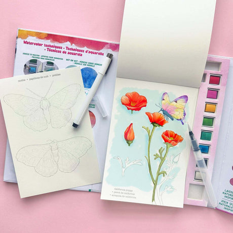 Art supplies for the Watercolor Journal Forest Flora kit including a notebook with butterfly design, watercolor set, and floral illustration on a pink background.