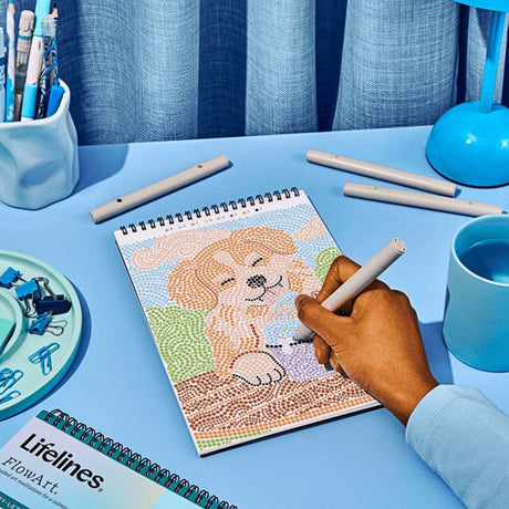 Person coloring a dog illustration on a spiral-bound notebook with markers on a blue table.