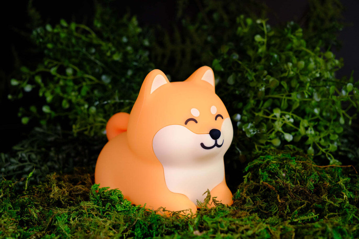 A World of Mushi Ambient Squishy Dog Light depicting a small orange and cream Shiba Inu dog figurine sitting on green moss with a dark green foliage background.