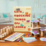 Board game 'Cats Knocking Things Off Ledges' with components on a wooden table.