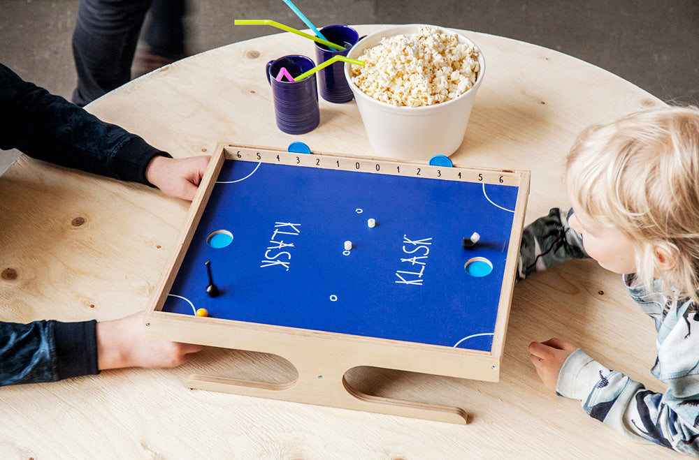Children playing KLASK - An Epic Magnetic Battle! Game on a round table with popcorn and straws.