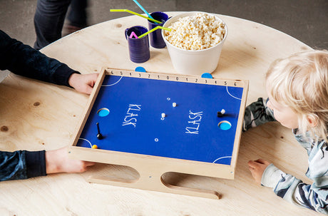 Children playing KLASK - An Epic Magnetic Battle! Game on a round table with popcorn and straws.