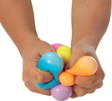 Colorful Teenie NeeDoh Rainboh being squeezed by hands on a white background