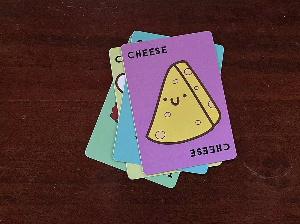 Stack of Taco Cat Goat Cheese Pizza cards with a purple card featuring a cheese wedge illustration on a dark brown background.