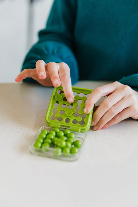 Person playing with a green IQ MINI Puzzle Game on a light surface.