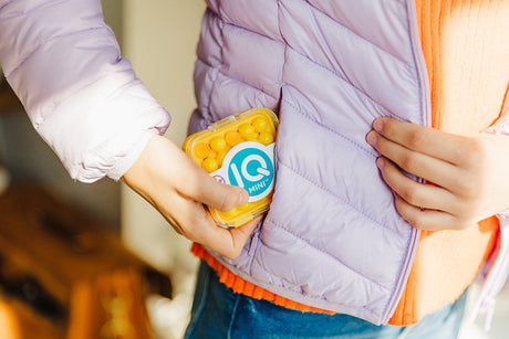 Person holding a container of IQ MINI Puzzle Game with a colorful jacket.