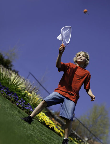 Child playing with a Djubi SlingBall Classic on  grass  with a clear blue sky.