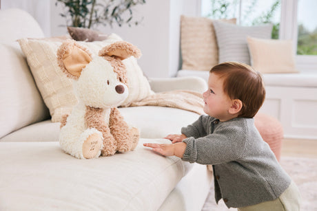 Child interacting with a Baby GUND Peeki the Puppy on a couch in a cozy living room.