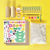 Craft supplies for Paper Mache All Day! including stickers, paper, straws, and paint on a yellow background