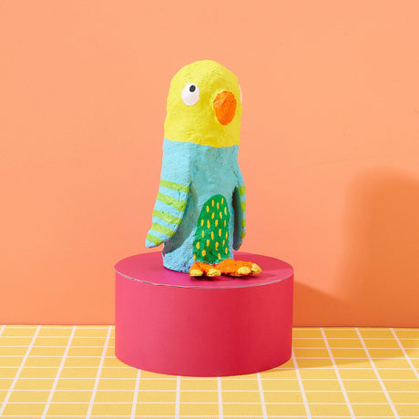 Colorful parrot-shaped toy on a pink platform with an orange background made with the Paper Mache All Day! kit