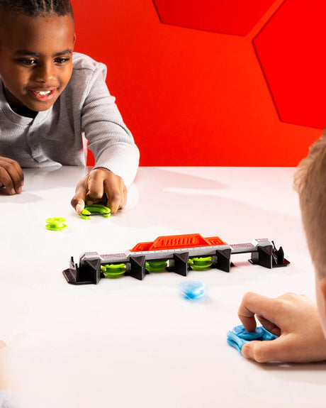 Two children playing with a Magshuto Knockout Rail on a white table against a red geometric-patterned wall.