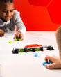 Two children playing with a Magshuto Knockout Rail on a white table against a red geometric-patterned wall.