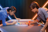 Two people playing Doteki Multiplayer Battle Pack on a table against a dark background with neon lights.