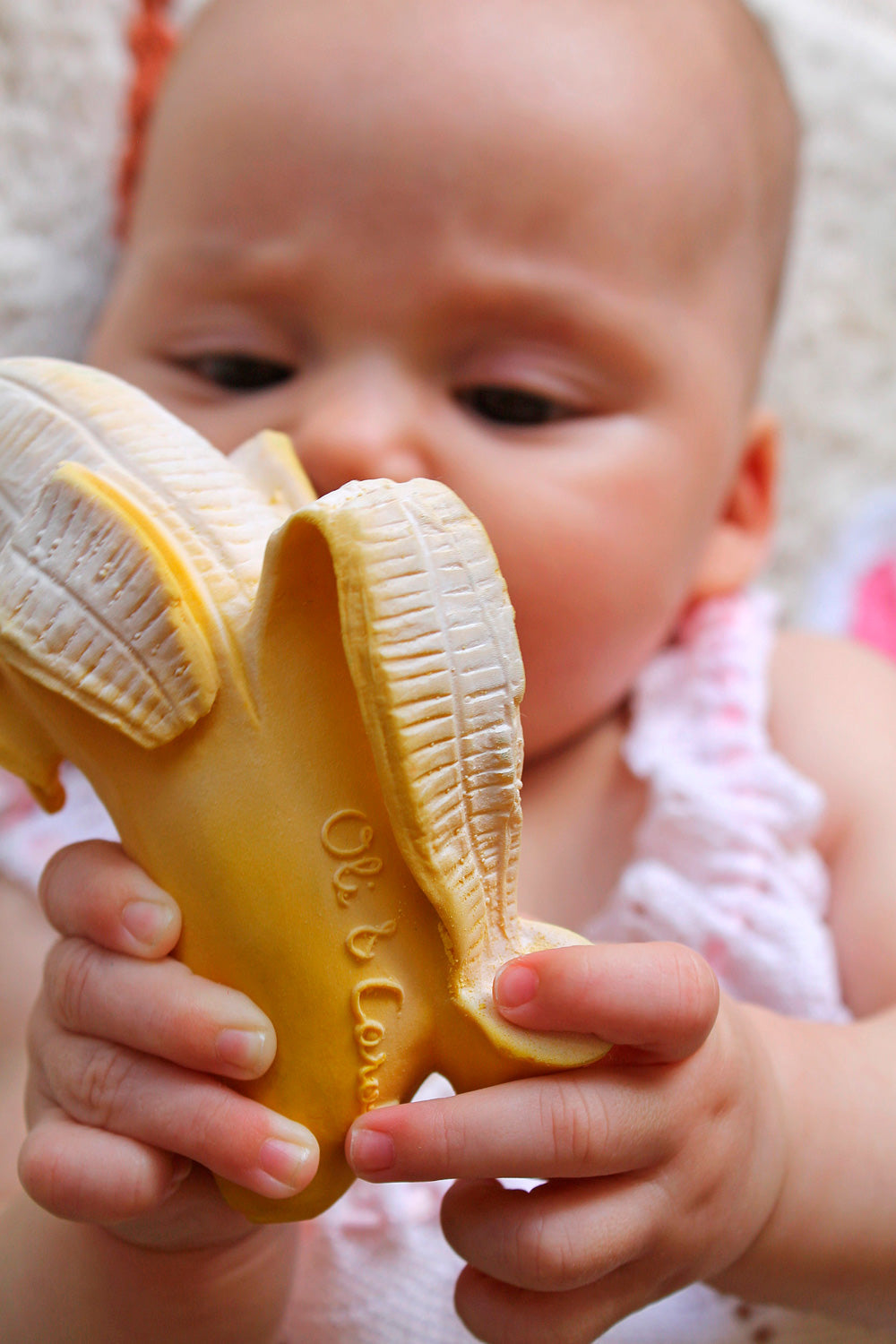 Baby holding a Oli & Carol Ana Banana Teether with a blurred background