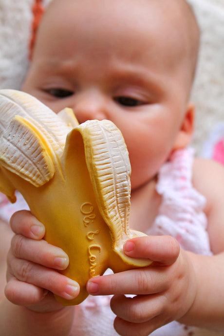 Baby holding a Oli & Carol Ana Banana Teether with a blurred background